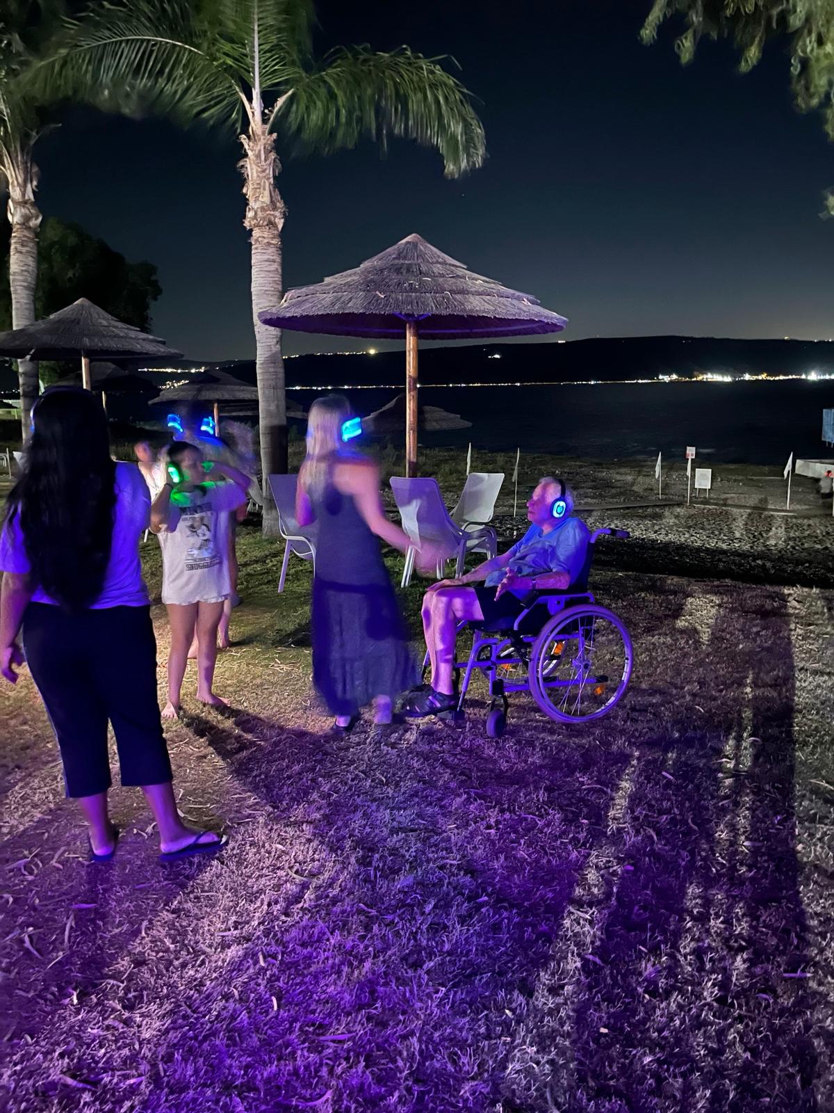 ריקודים בלילה מול הכנרת עם אוזניות זוהרות ואורח בכיסא גלגלים